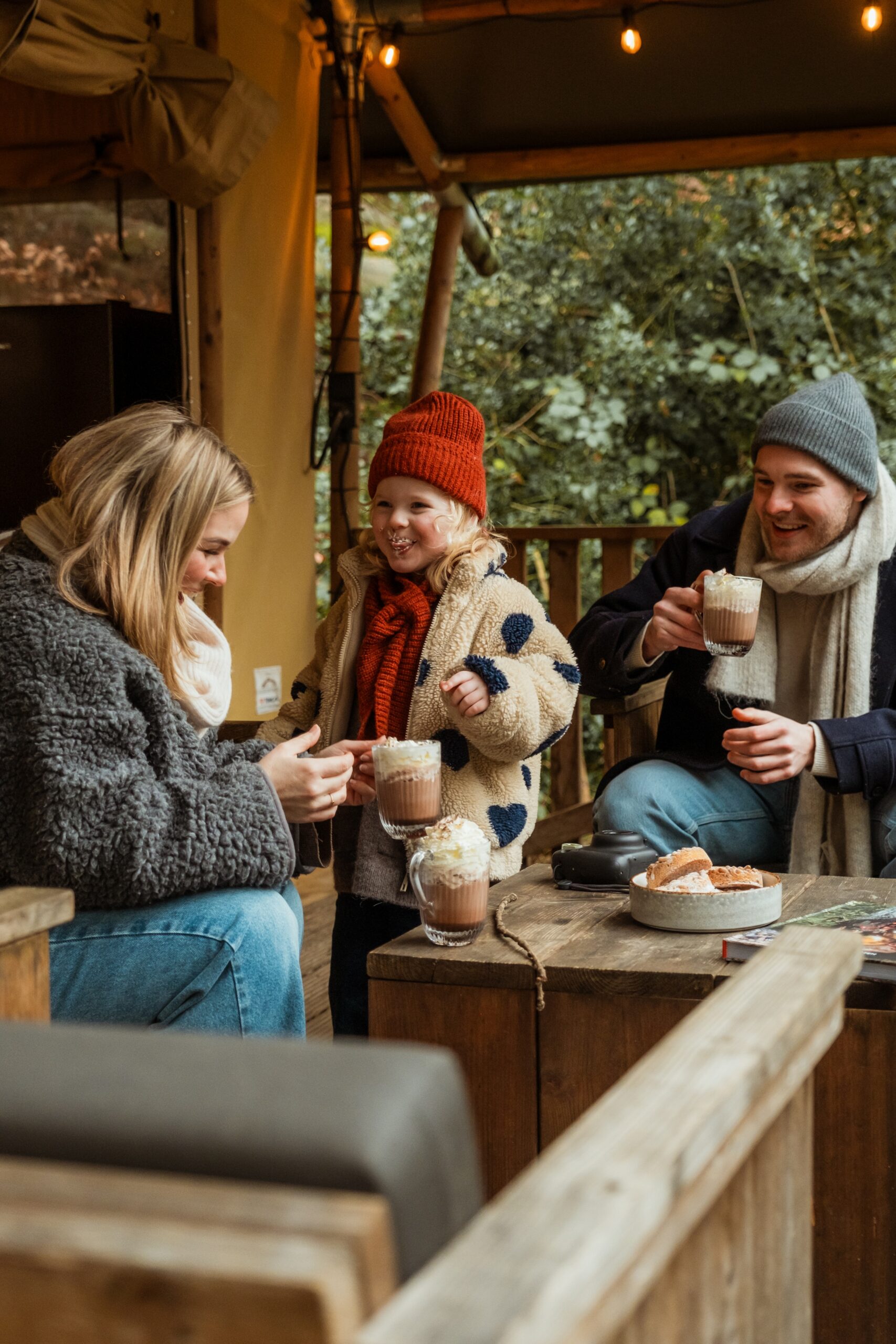 Gezin drinkt warme chocomelk op de veranda van een lodgetent op Buitenplaats Beekhuizen