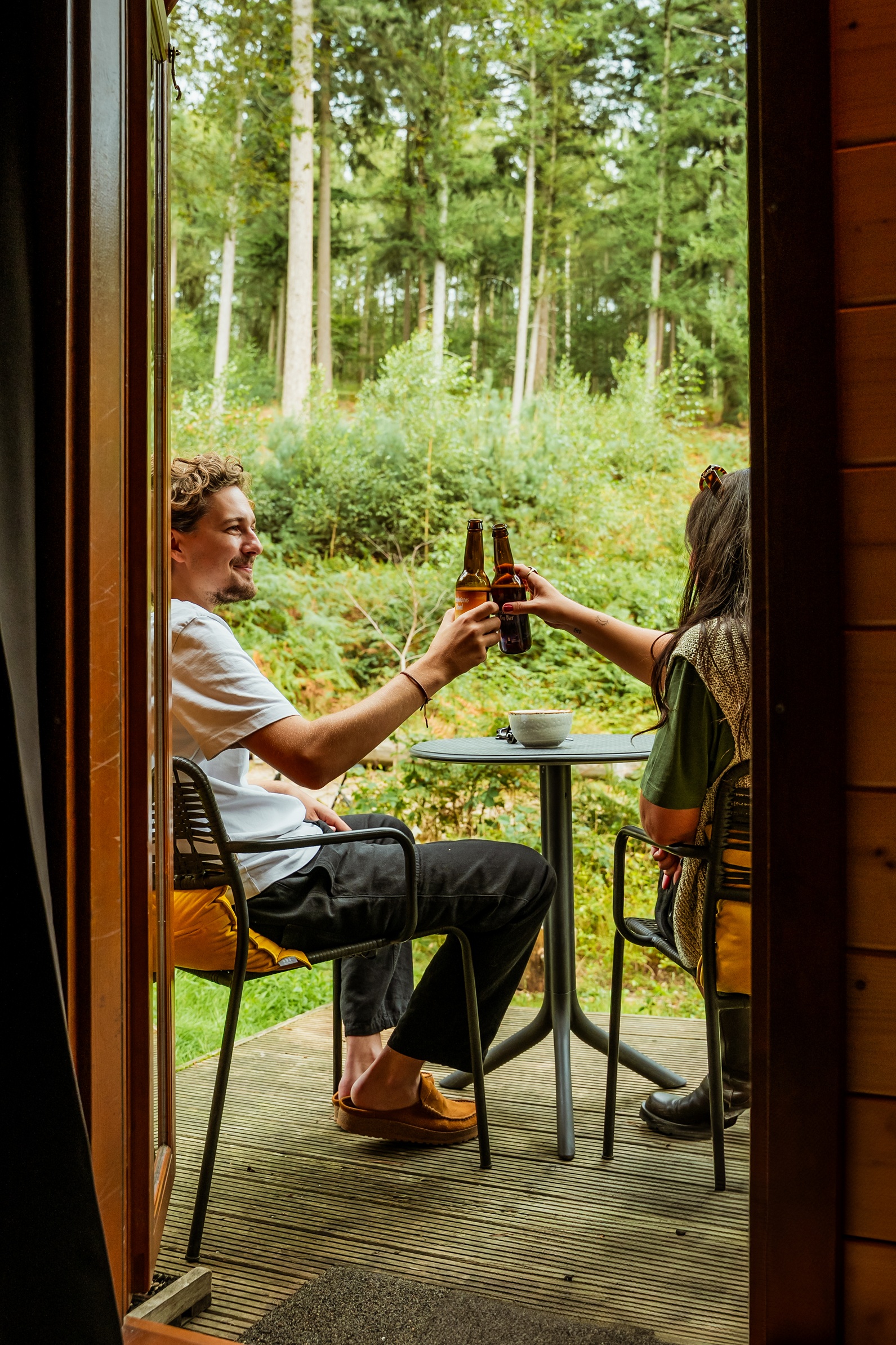 Een man en een vrouw borrelen op de vlonder voor een Pod en proosten met elkaar